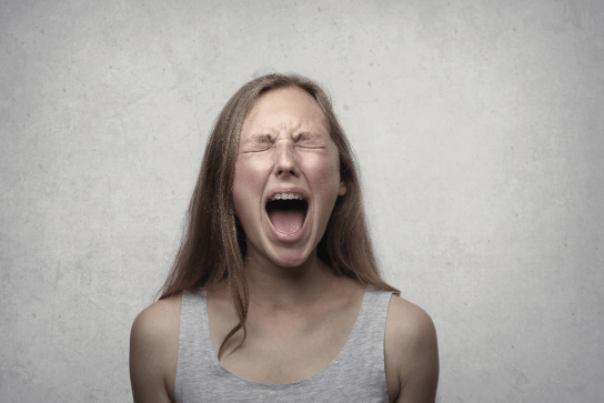A woman in a grey tank top screaming in anger.